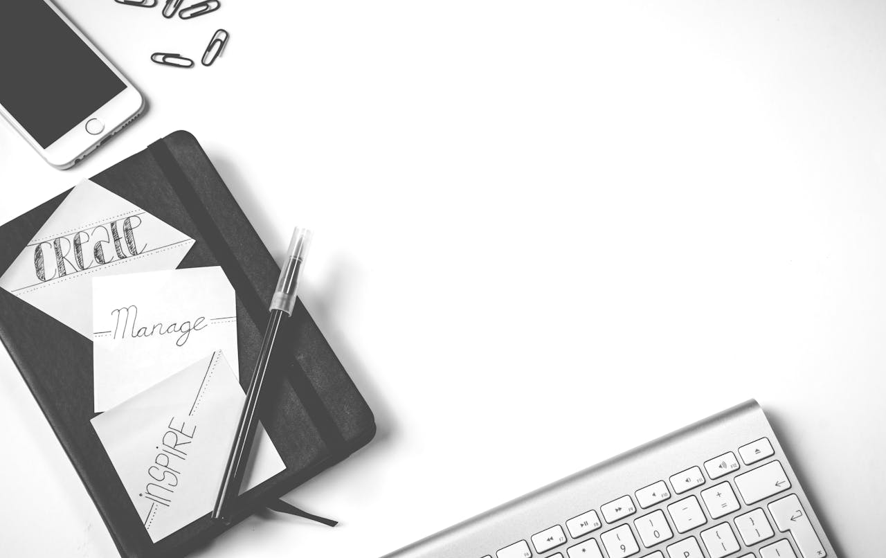 about-img Minimalist flat lay of an office desk with notebook, keyboard, and smartphone.